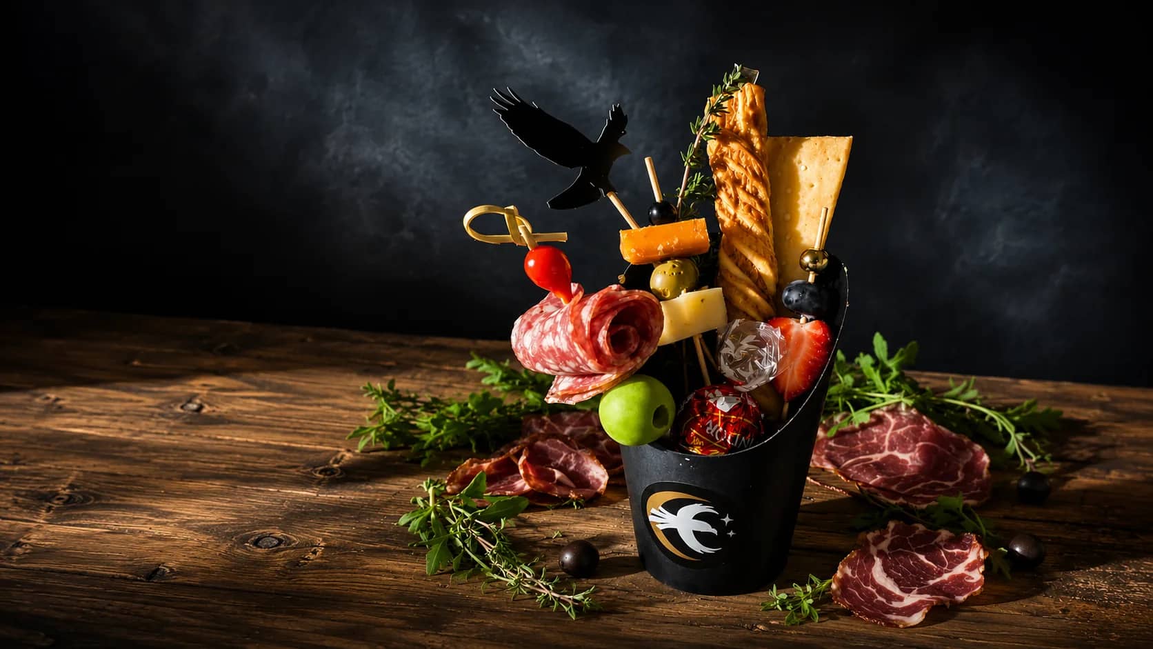 A signature Cured Crow charcuterie cup filled with cured meats, artisan cheeses, crackers, and fruit on a rustic table